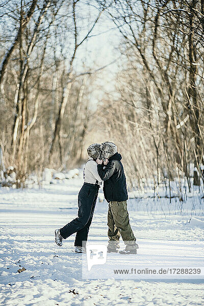 Mid adult couple kissing each other while standing on snow path in forest