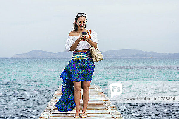 Lächelnde Frau  die ein Smartphone benutzt  während sie auf einem Steg steht