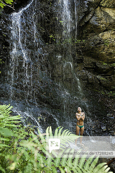 Junge schöne Frau im Bikini wäscht sich unter einem kleinen plätschernden Wasserfall