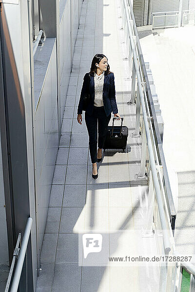 Weibliche Unternehmerin schaut weg  während sie mit einem Koffer durch einen Gebäudeflur geht