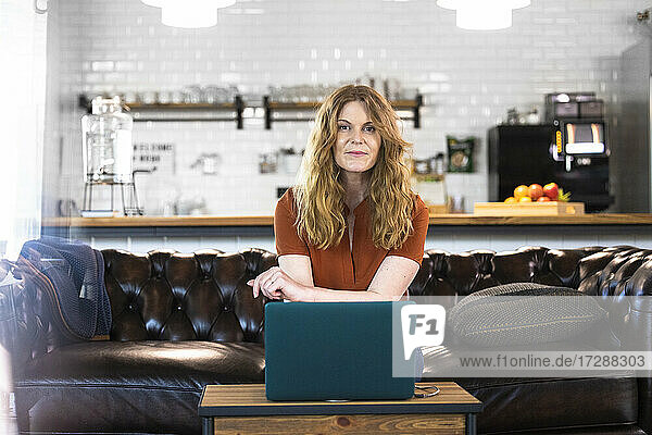 Businesswoman with laptop sitting on sofa at office cafeteria