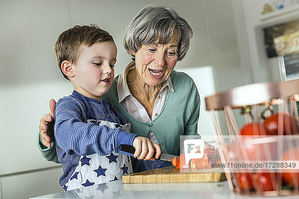 Enkel schneidet Tomate bei Großmutter in der Küche