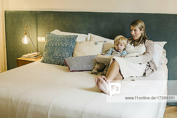 Schwangere Frau im Gespräch mit ihrem Sohn  während sie ein Fotoalbum auf dem Bett zu Hause zeigt