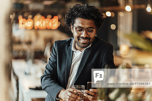 Smiling male professional text messaging through smart phone in cafe