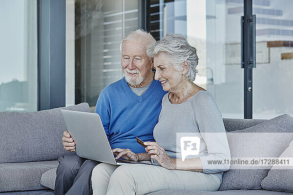 Smiling senior couple doing online shopping while sitting in living room at home