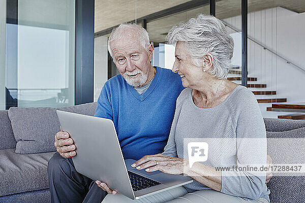 Senior couple with laptop sitting on sofa in living room