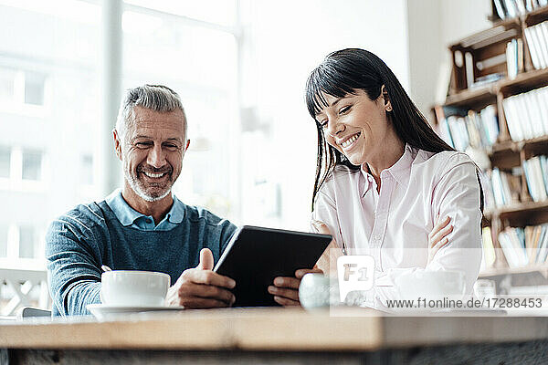 Lächelnder Geschäftsmann  der ein digitales Tablet von einem Kollegen in einem Café benutzt