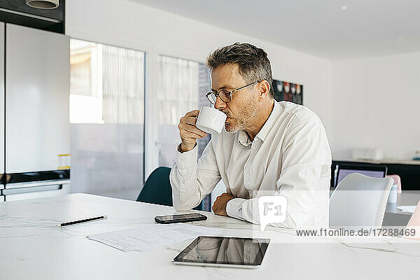 Geschäftsmann trinkt Kaffee  während er an der Kücheninsel im Heimbüro sitzt