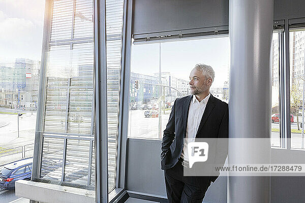 Businessman with hands in pockets leaning on column at office