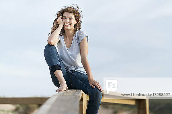Lächelnde Frau mit Kopf in der Hand auf dem Geländer vor dem Himmel sitzend