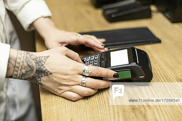 Young tattooed female cashier using credit card reader at checkout in bar