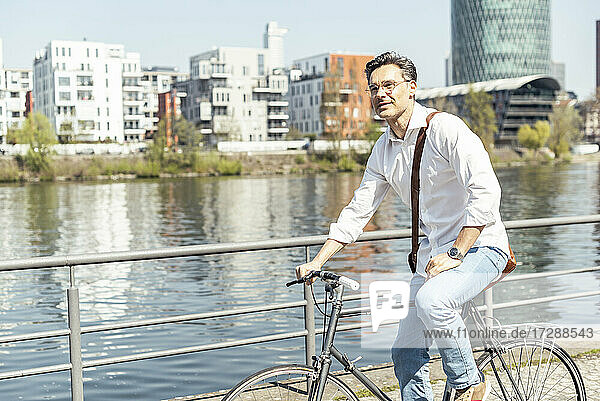 Mature male entrepreneur on bicycle by river on sunny day