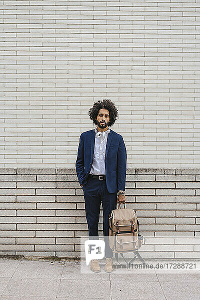 Männlicher Unternehmer  der einen Rucksack hält  während er mit der Hand in der Tasche auf dem Fußweg steht