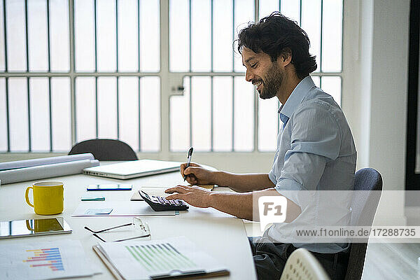 Lächelnder junger Geschäftsmann  der am Schreibtisch im Büro sitzt und arbeitet
