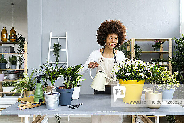 Lächelnde Blumenhändlerin mit Gießkanne neben Pflanzen im Laden stehend