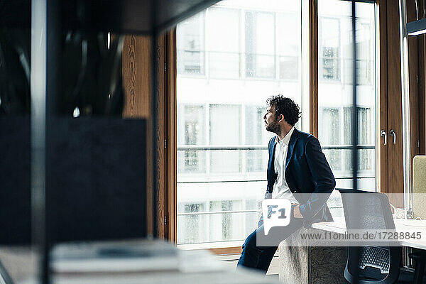 Thoughtful male entrepreneur looking away while sitting on desk