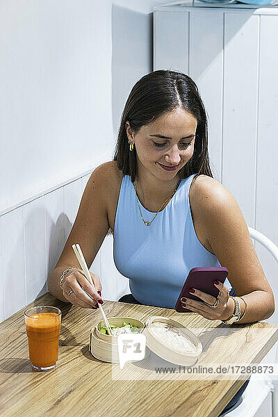 Lächelnde Frau benutzt ihr Smartphone beim Essen im Restaurant