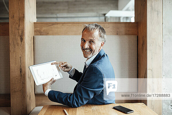 Lächelnder Geschäftsmann zeigt Geschäftsplan auf digitalem Tablet im Büro
