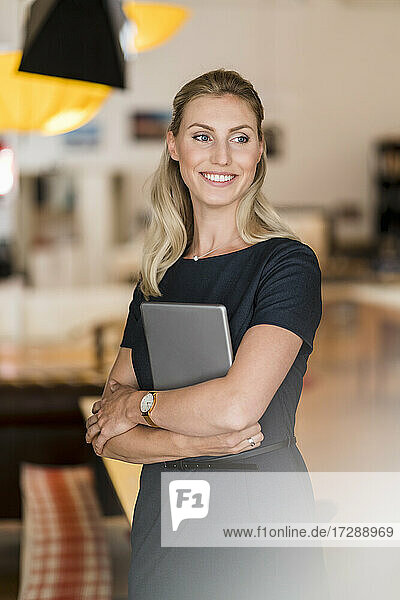 Lächelnde schöne Unternehmerin  die im Büro ein digitales Tablet hält und dabei wegschaut