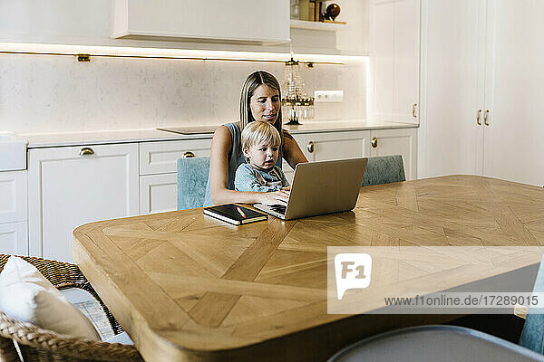 Geschäftsfrau mit Sohn arbeitet am Laptop am Esstisch in der Küche