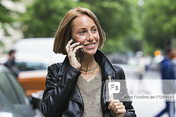 Lächelnde Frau  die wegschaut  während sie mit einem Smartphone telefoniert