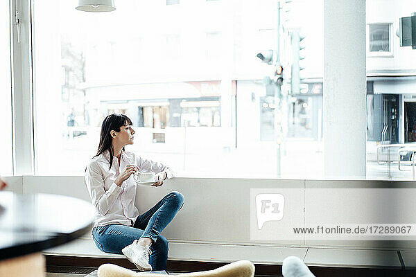 Unternehmerin sitzt mit Kaffeetasse am Fenster eines Cafés
