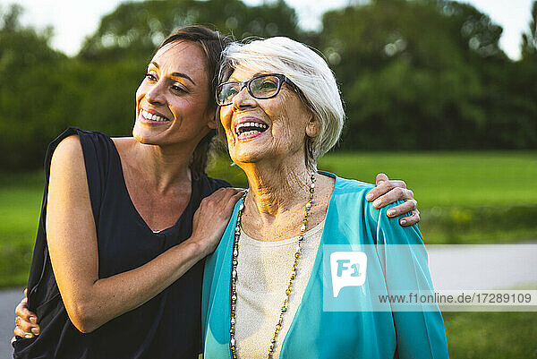 Enkelin lächelt  während sie mit dem Arm um ihre Großmutter im Park steht