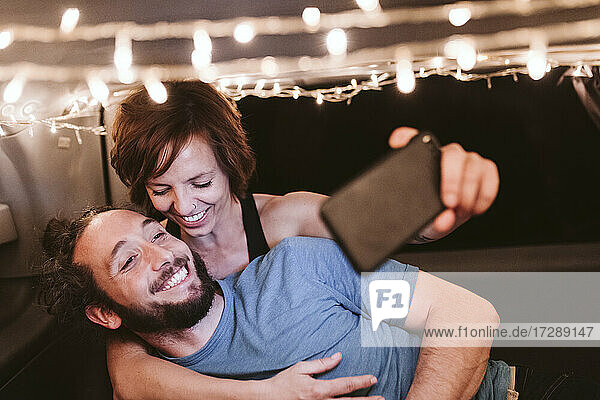 Lächelndes Paar macht Selfie in beleuchtetem Van bei Nacht