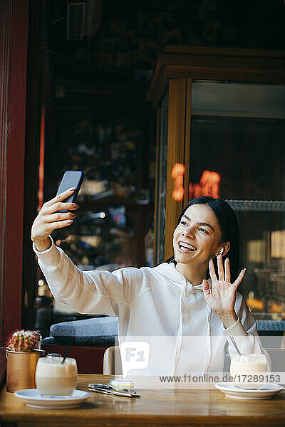 Smiling woman waving on video call at coffee shop