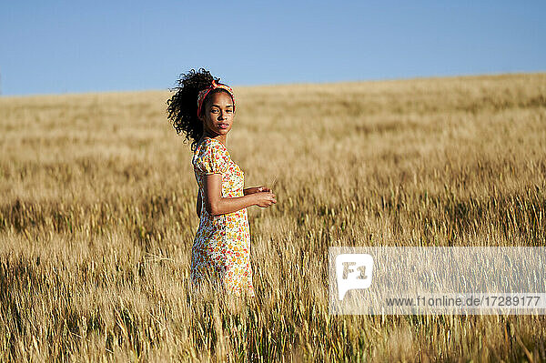 Junge Frau mit lockigem Haar steht an einem sonnigen Tag in einem Weizenfeld