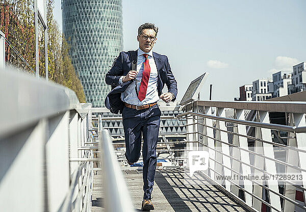 Businessman with backpack running on footpath