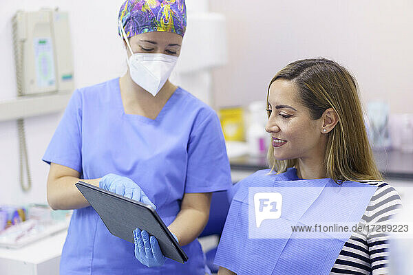 Eine Zahnärztin mit Gesichtsschutzmaske zeigt einem Patienten in einer medizinischen Klinik ein digitales Tablet