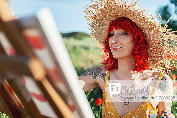 Lächelnde tätowierte Frau mit roten Haaren malt an einem sonnigen Tag