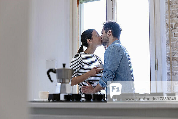 Pärchen küsst sich am Fenster in der Küche zu Hause