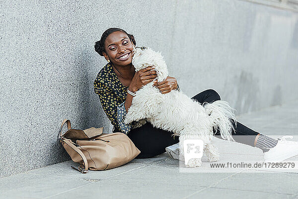 Lächelnde Frau  die mit ihrem Hund spielt  während sie auf dem Gehweg sitzt