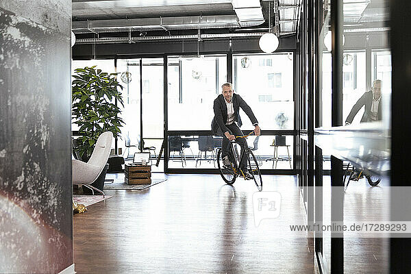 Männlicher Unternehmer fährt Fahrrad im Büro