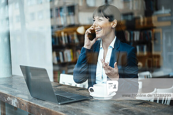 Reife Unternehmerin mit Laptop  die in einem Café mit ihrem Mobiltelefon spricht