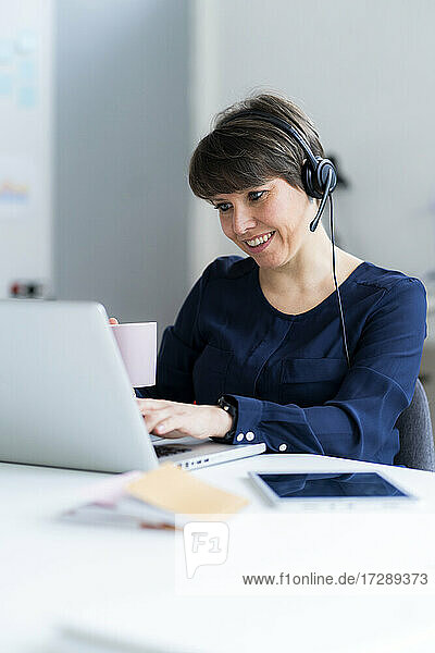 Smiling businesswoman wearing headset using laptop while working in office