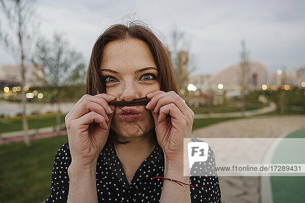 Verspielte reife Frau macht Schnurrbart mit Haaren im Park