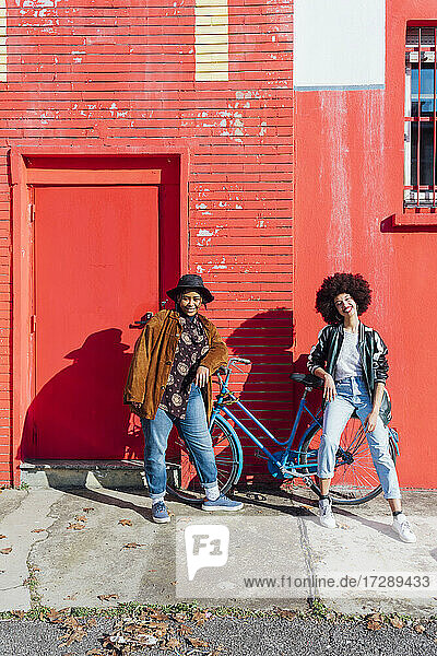 Lächelnde Freunde lehnen sich auf einem Fahrrad vor einem roten Gebäude