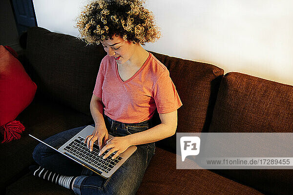Junge Frau tippt auf dem Sofa zu Hause auf einem Laptop