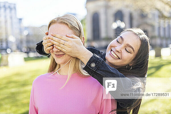 Lächelnde Frau  die die Augen ihrer Freundin im Park schließt