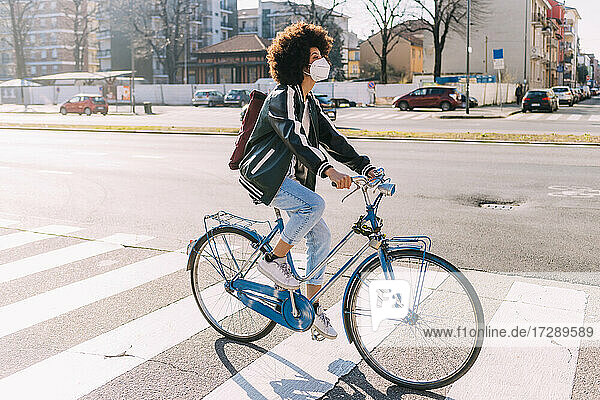 Young woman with face mask and backpack riding bicycle in city