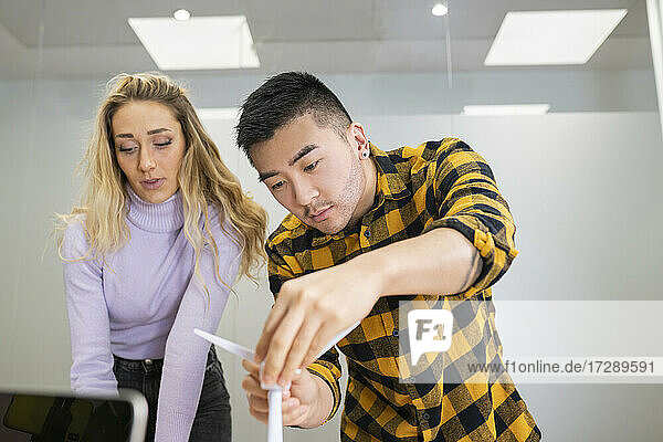 Junge männliche Fachkraft  die eine Windkraftanlage einstellt  während sie neben einer weiblichen Kollegin im Büro steht