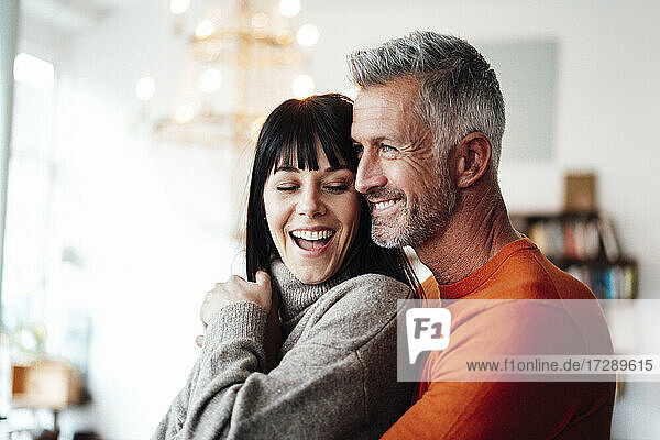 Smiling man embracing woman while looking away at cafe