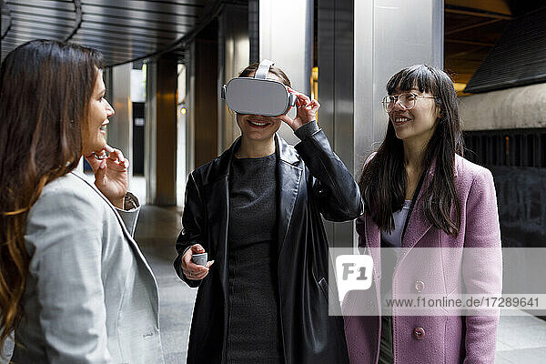 Lächelnde Kollegen  die eine Geschäftsfrau mit einem Virtual-Reality-Headset auf dem Gehweg betrachten