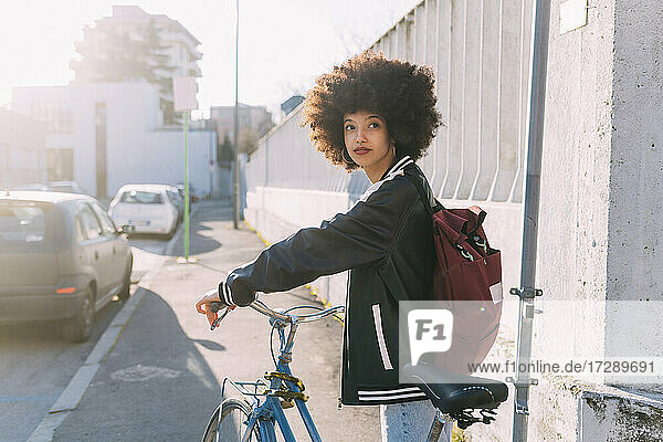 Junge Afro-Frau mit Rucksack und Fahrrad auf dem Fußweg stehend