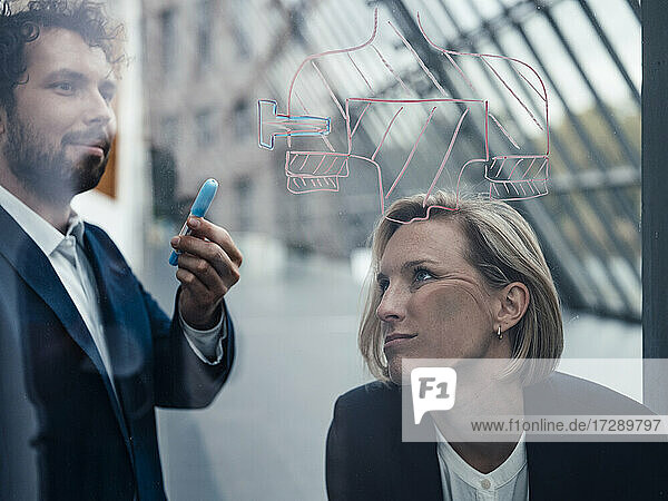 Gelangweilte Geschäftsfrau lehnt an einer Glaswand  während ein Geschäftsmann ein Diagramm im Büro bespricht