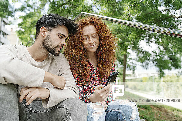 Young couple using smart phone together in park