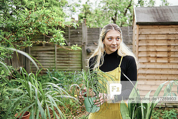 Blonde Frau mit Topfpflanze schaut weg  während sie im Hinterhof steht